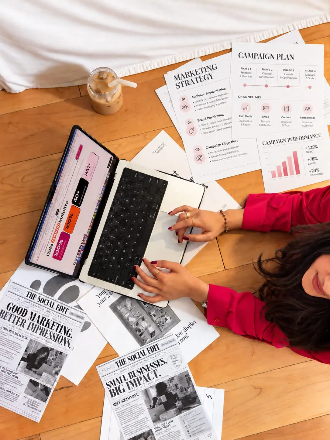 Overhead view of a SocialSaiya strategist at a laptop surrounded by marketing strategy, campaign plan and Social Edit printouts