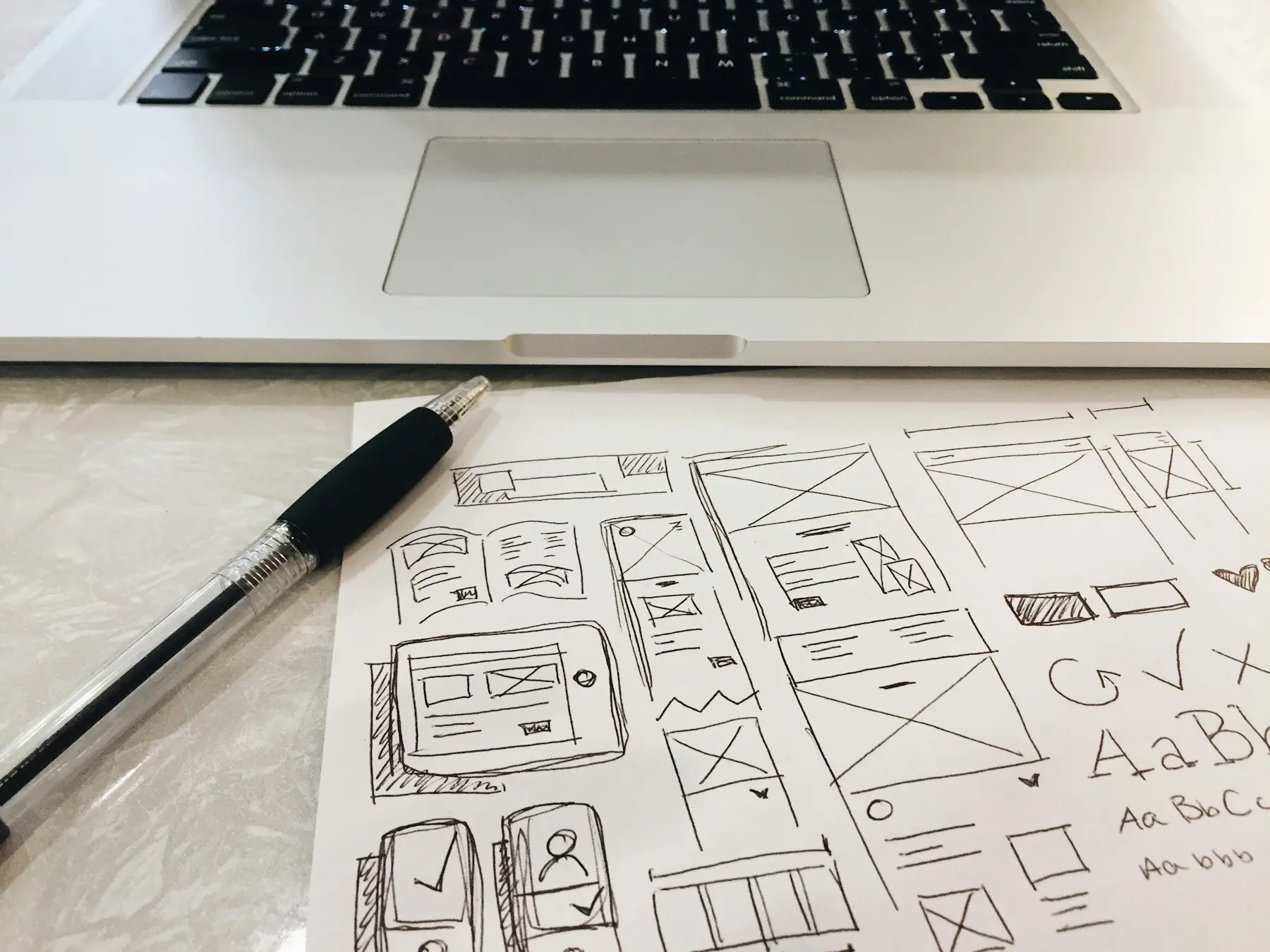 Hand-drawn website wireframe sketches on paper in front of a laptop